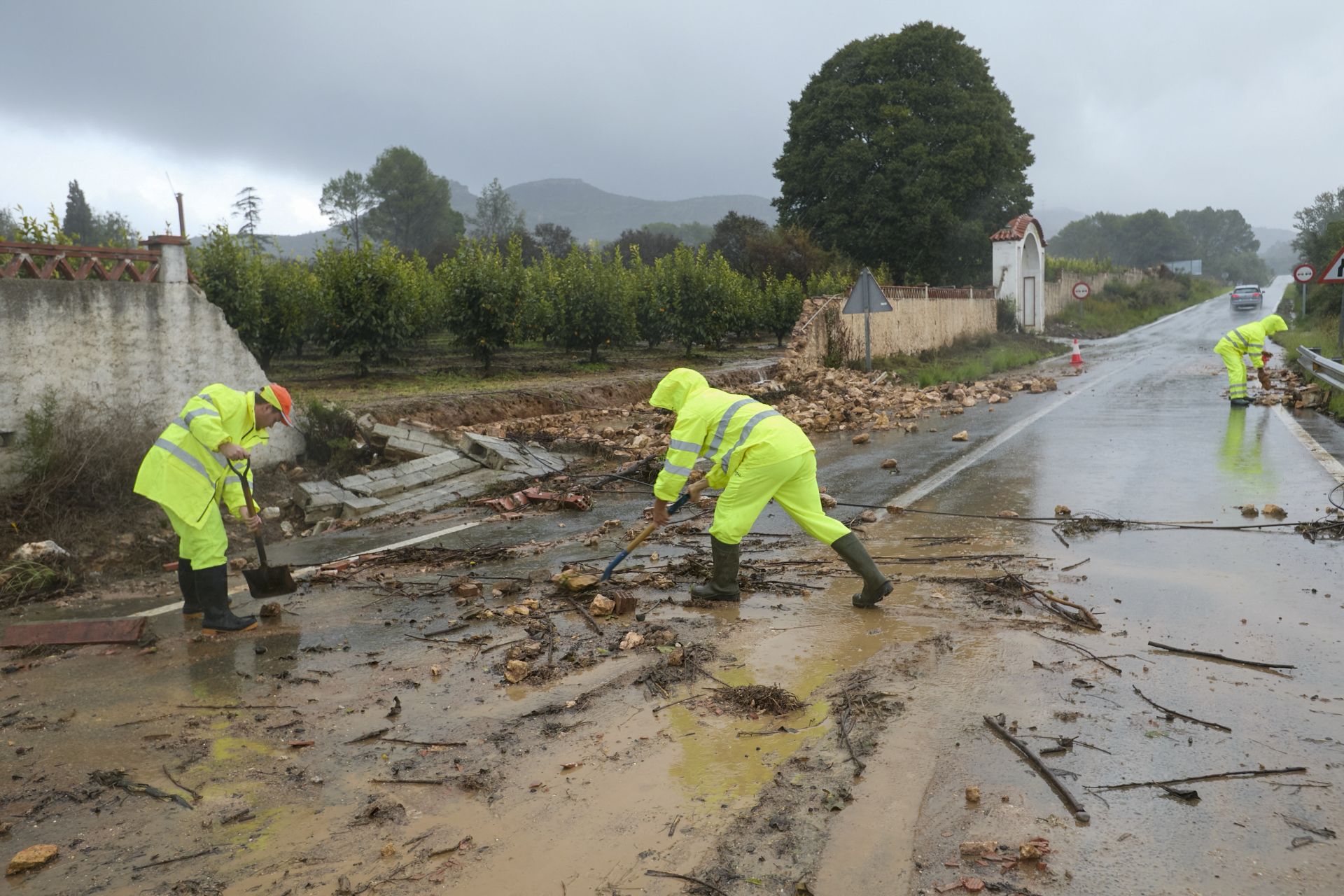 Unos operarios limpian la carretera de acceso a Manuel cortada debido a las lluvias torrenciales que afectan a la Comunitat Valenciana