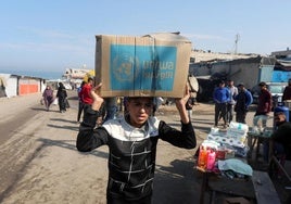 Un joven palestino carga un paquete con ayuda humanitaria proporcionada por la UNRWA en Gaza.