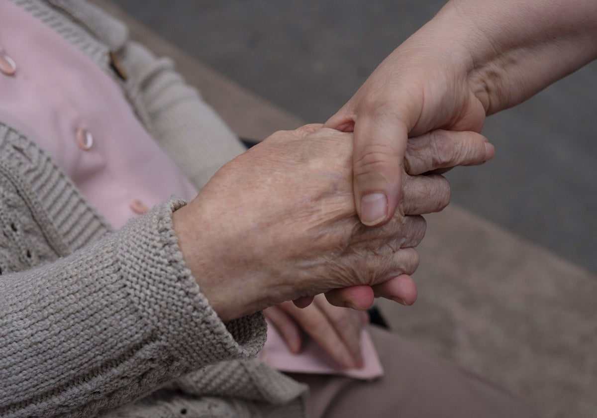 Una cuidadora coge de la mano a su familiar enferma.