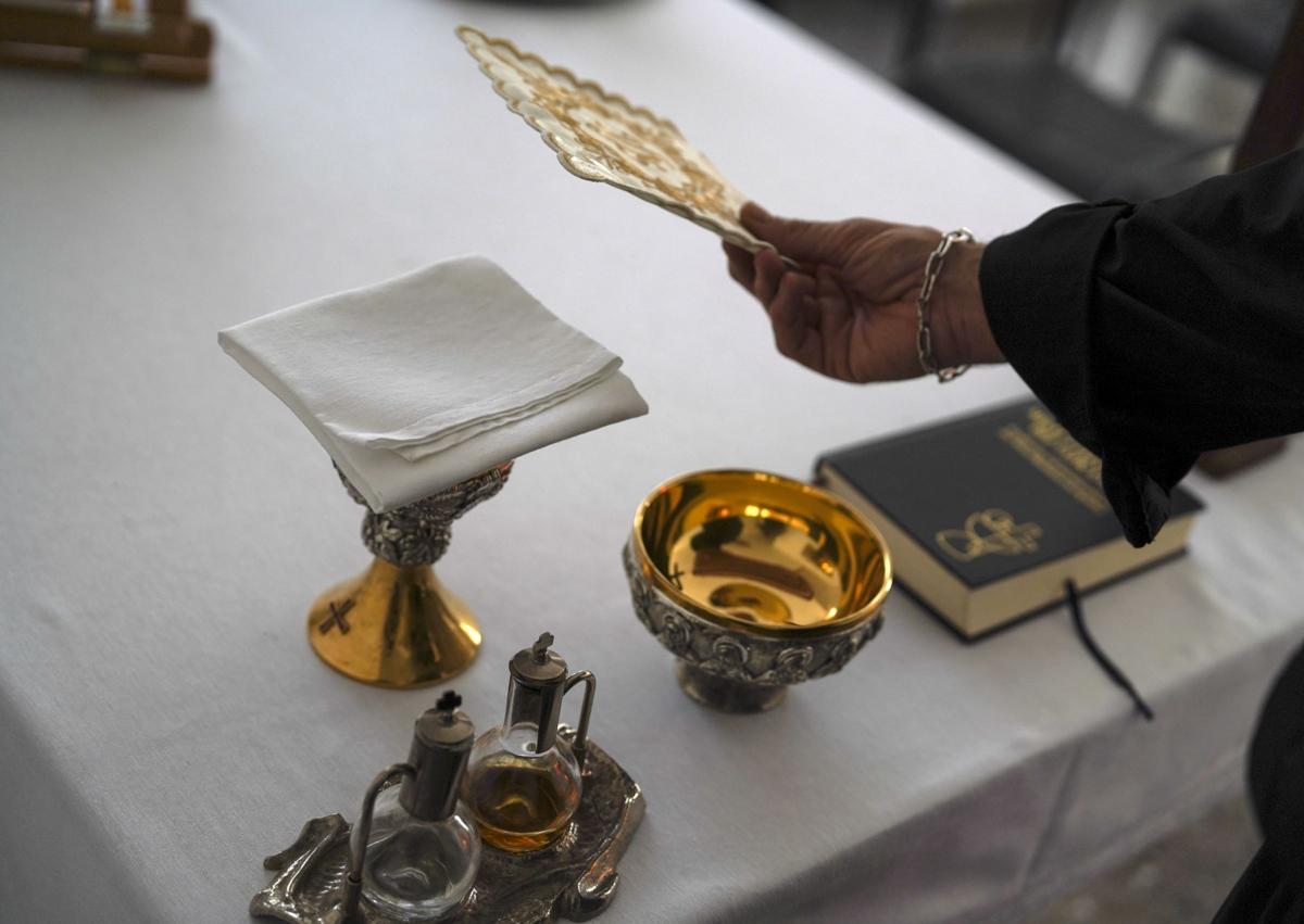 Imagen secundaria 1 - El cura de San Ramón, en la iglesia reconvertida en un centro logístico de reparto de ayuda; Un detalle del corporal completamente blanco cubriendo el cáliz, tal y como se lo encontró el párroco en la sacristía inundada de barro; Aspecto de la sacristía al día siguiente de la DANA con la imagen del corporal y el cáliz encima de una mesita.