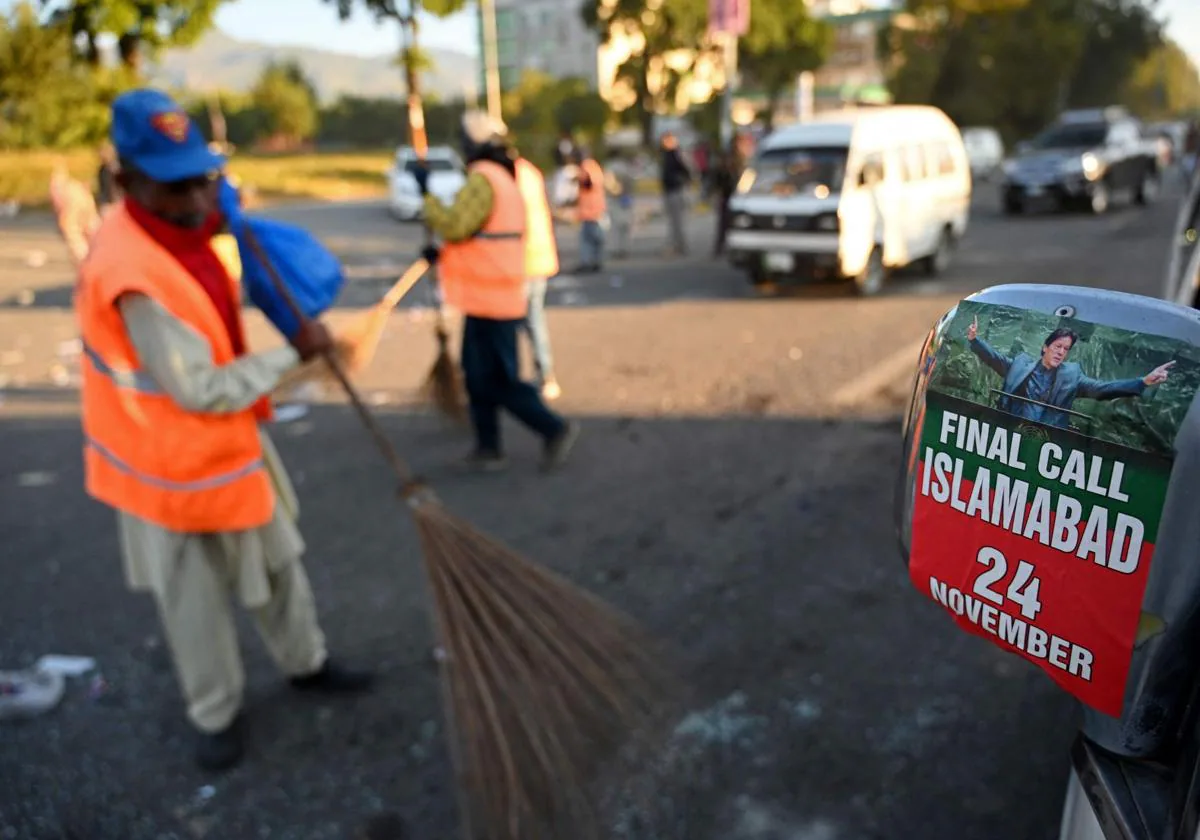 Trabajadores municipales limpian las calles de Islamabad tras los altercados del martes, en medio de vehículos averiados durante las protestas.