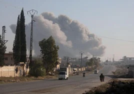 Unos combatientes entran en motocicletas en el distrito de Rashidin, en las afueras de Alepo, con el humo de una explosión de fondo.