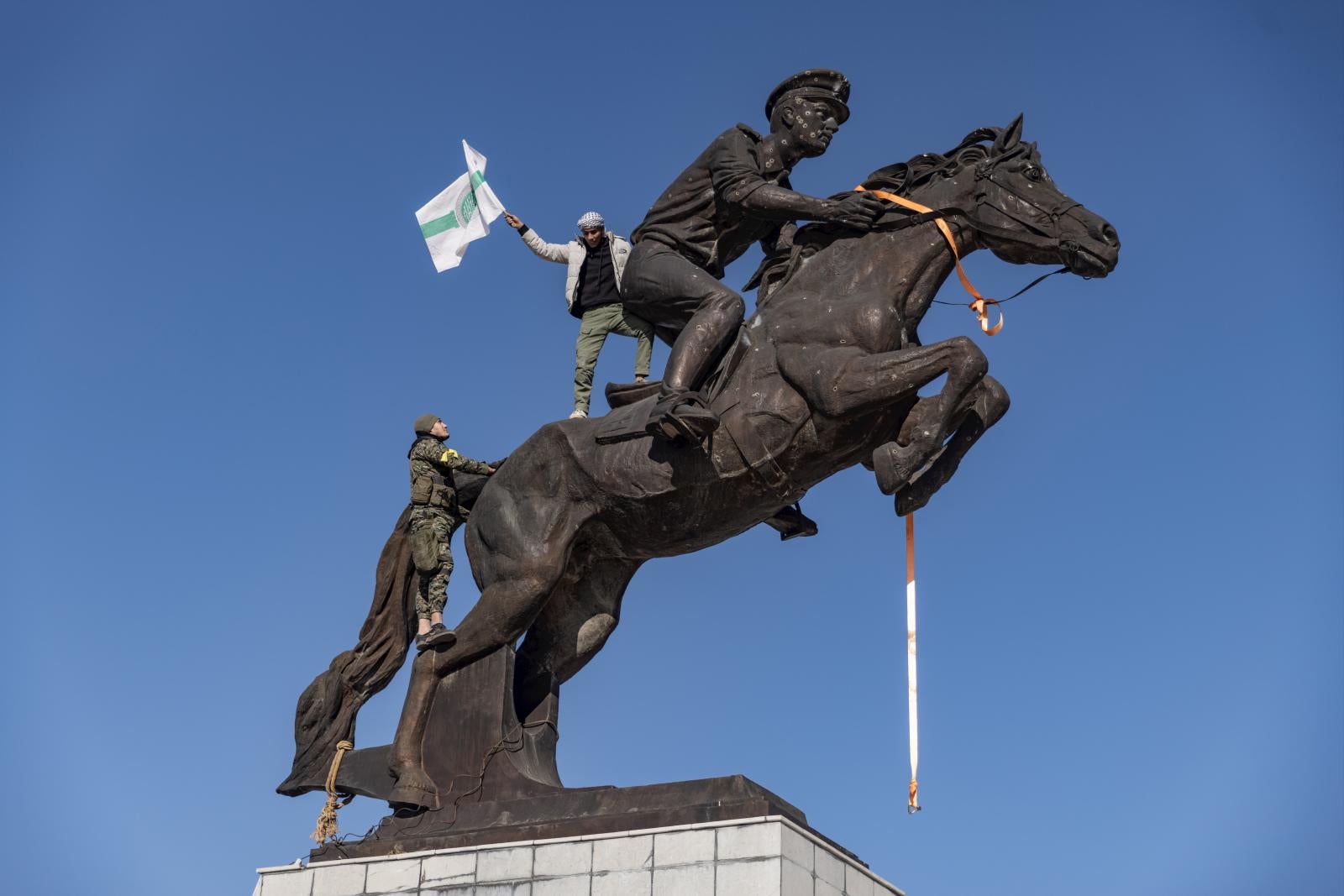 Un insurgente ondea una bandera encaramado a la estatua de Bassel al Assad antes de su derribo en Alepo.