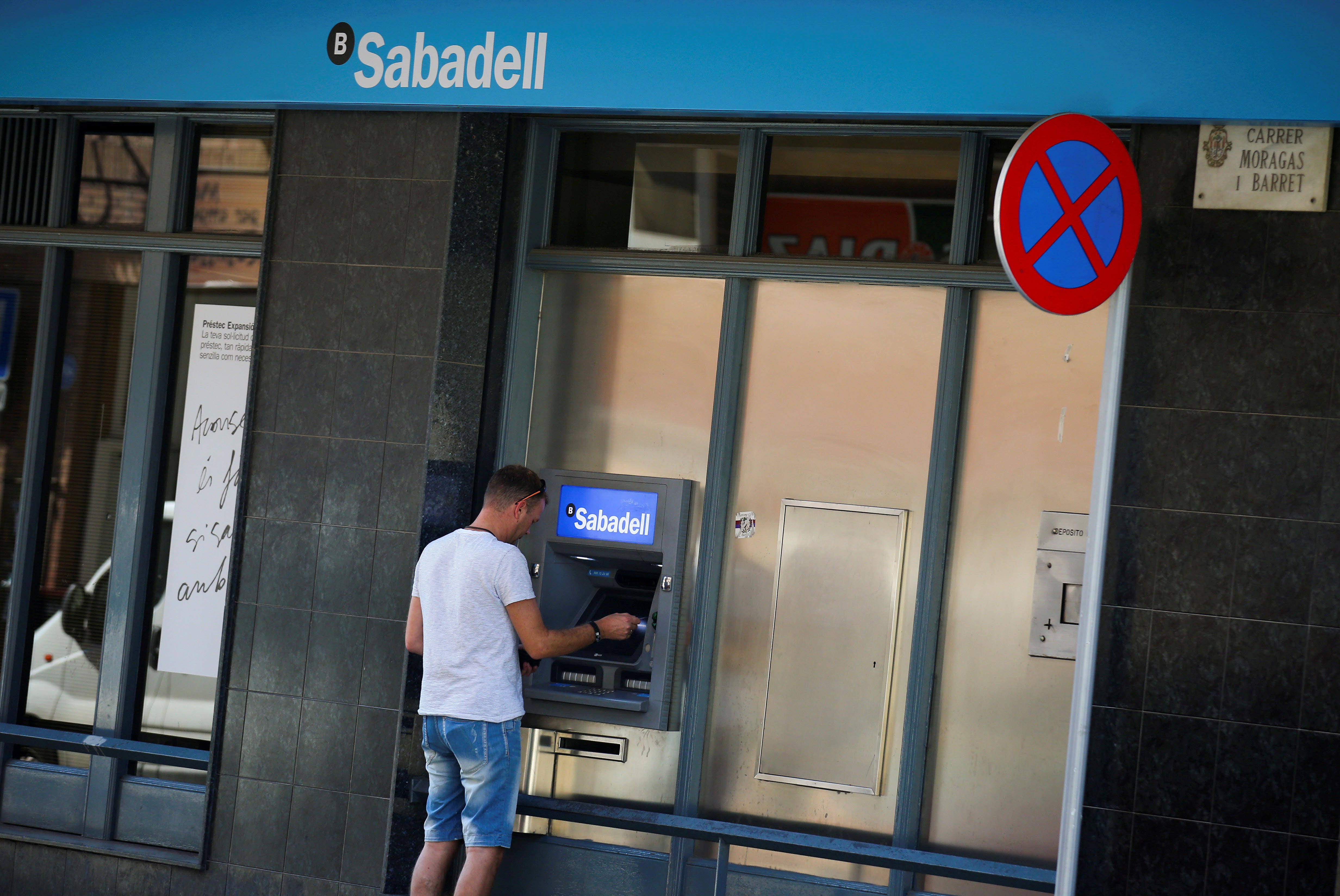 Hombre saca dinero de un cajero automático del Banco Sabadell.