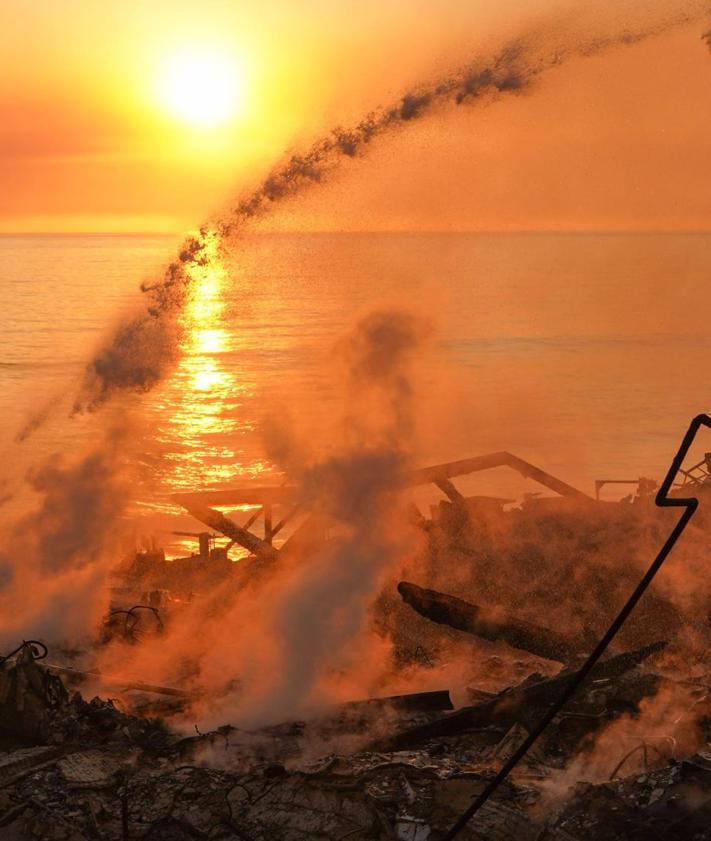 Imagen secundaria 2 - Arriba, la vista aérea de Pacific Palisades, totalmente reducido a escombros. En el medio, un residente observa desde la acera las llamas que devoran las montañas, y abajo, una vivienda destruida al lado de la playa. 