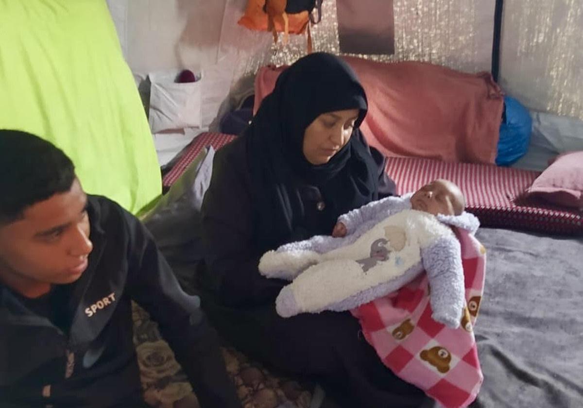 Fátima arrulla al menor de sus cinco hijos, que se refugian junto a ella en un precario campamento de Gaza.