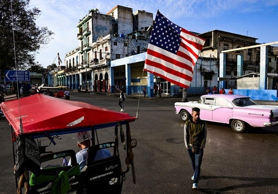 Un hombre camina junto a un triciclo utilizado como taxi y decorado con la bandera estadounidense en La Habana