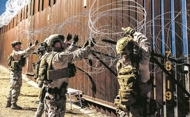 Marines estadounidenses refuerzan la alambrada en el muro para complicar el salto de migrantes ilegales.