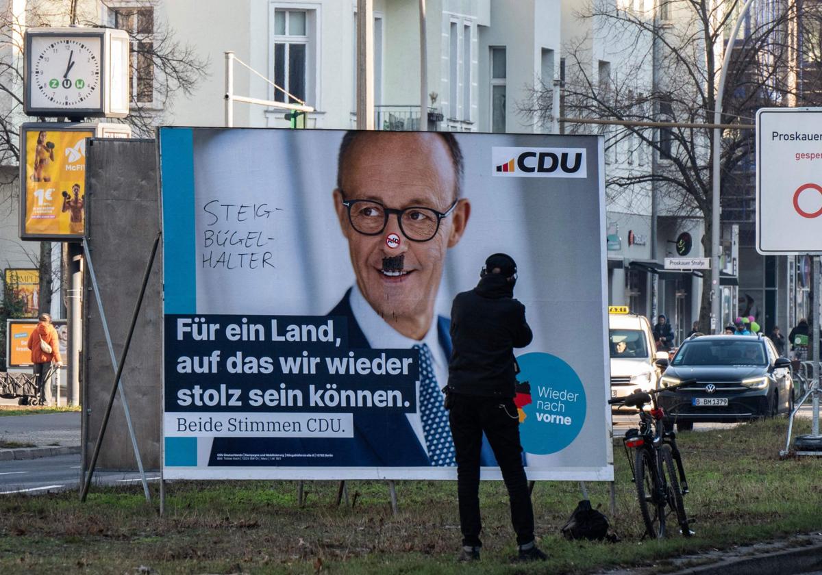 Un hombre toma una fotografía de un cartel de campaña electoral desfigurado del candidato de la Unión Demócrata Cristiana (CDU), Friedrich Merz, en Berlín.