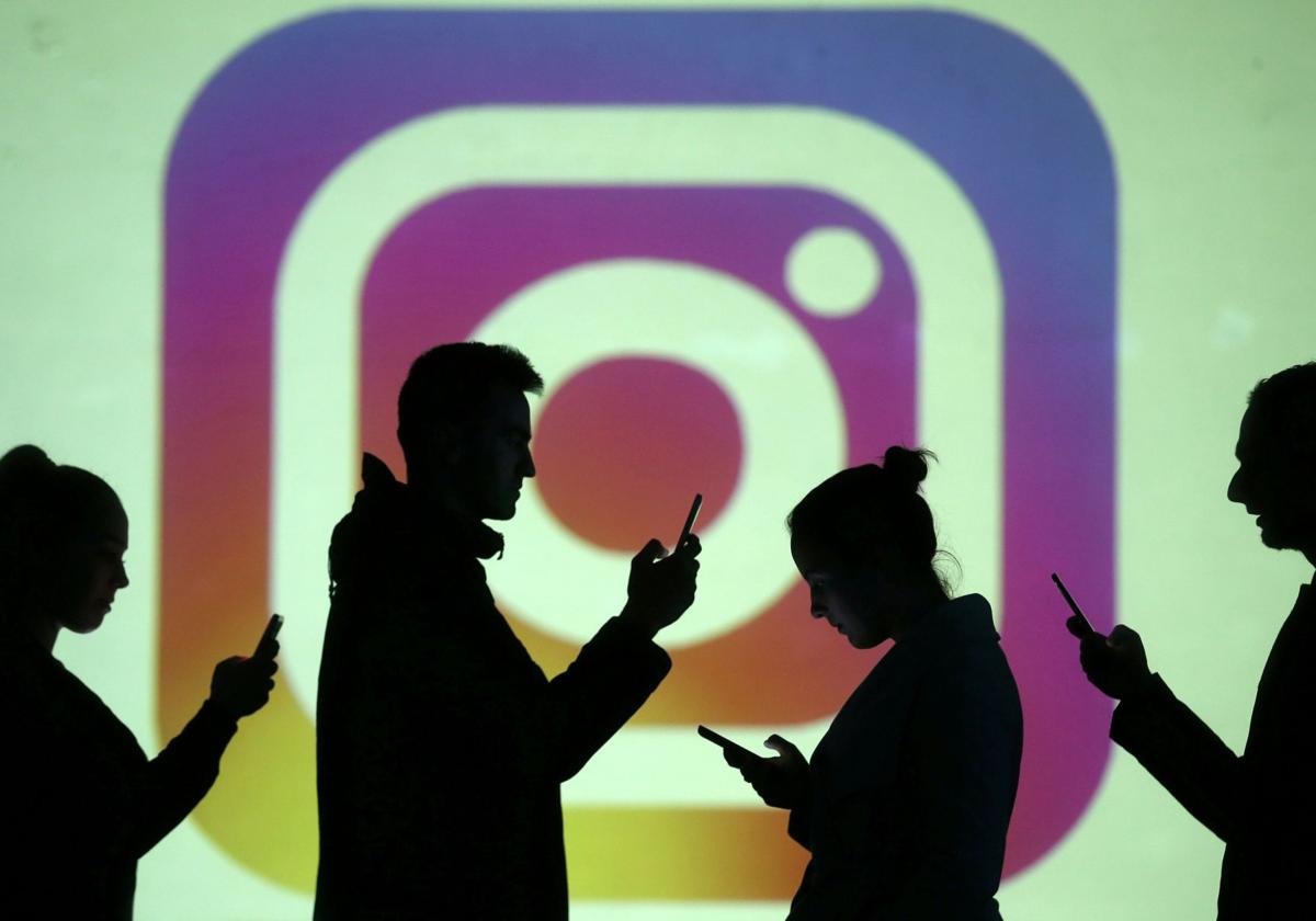 Siluetas de usuarios de dispositivos móviles frente a una proyección del logotipo de Instagram.