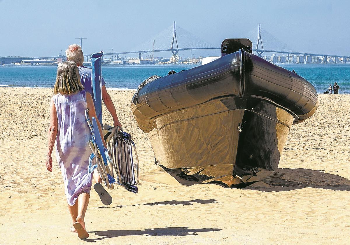 Dos turistas pasan junto a una narcolancha varada en la playa de Valdelagrana, en Cádiz.