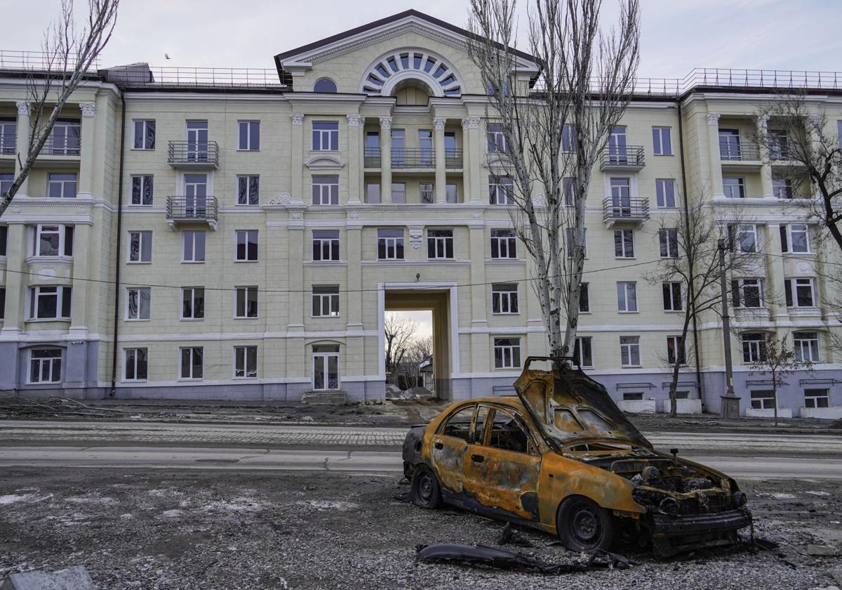 Un coche quemado en la acera frente a un edificio de apartamentos restaurado en Mariúpol, región de Donetsk.