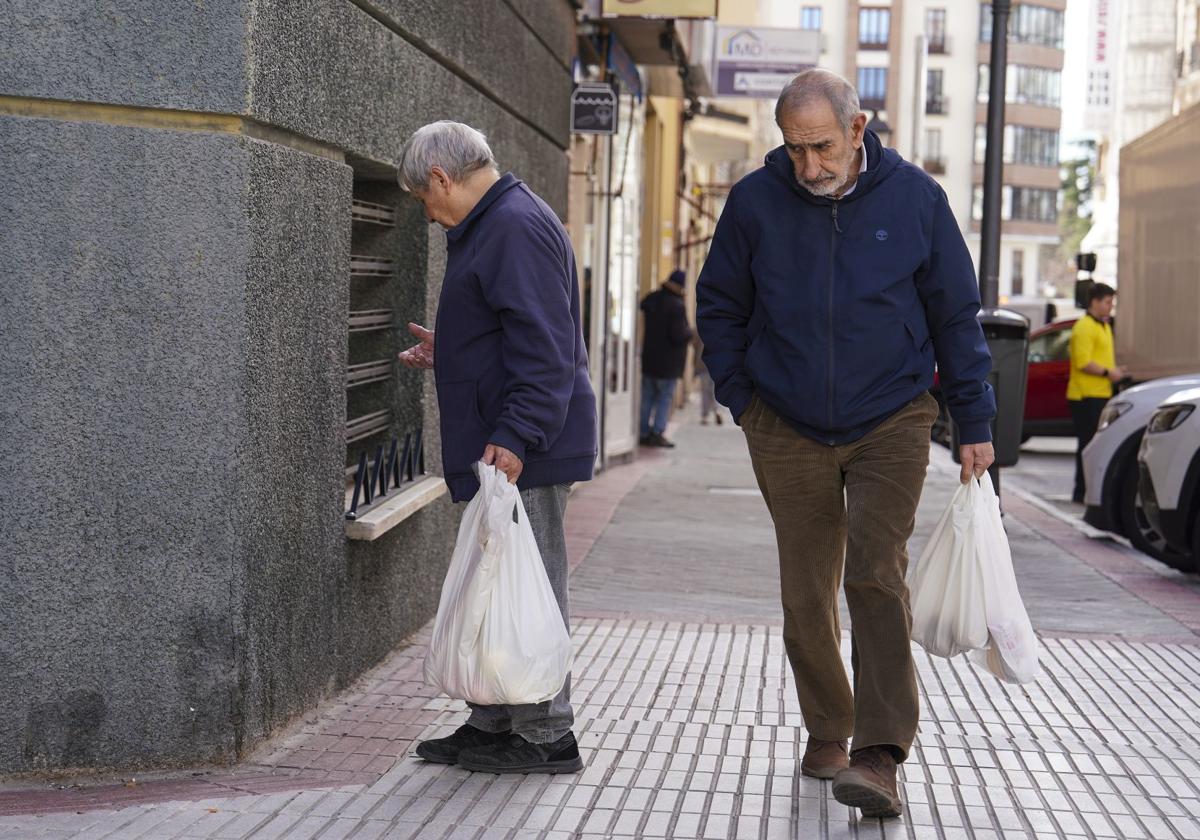 Dos jubilados caminan por la calle con bolsas de la compra.