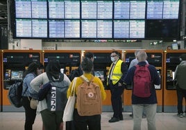 Varios pasajeros miranlos paneles de salidas y llegadas en Sans.