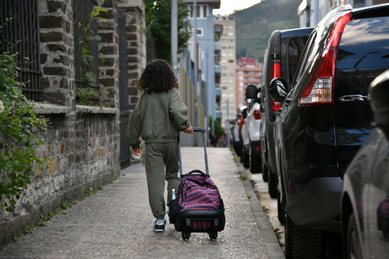 Una niña pasea por la calle con su mochila de ruedas