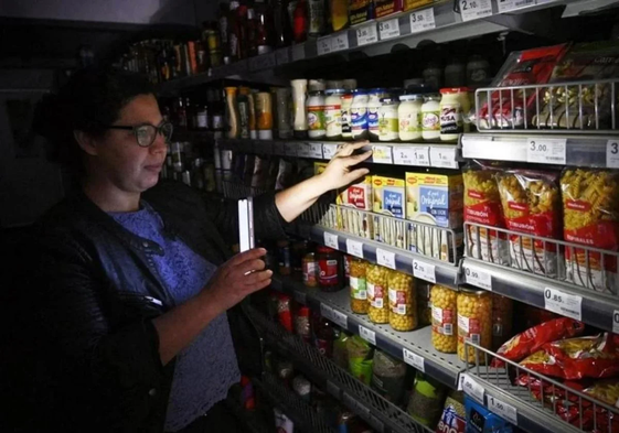 Una clienta ilumina las estanterías de un supermercado con su móvil. durante el apagón