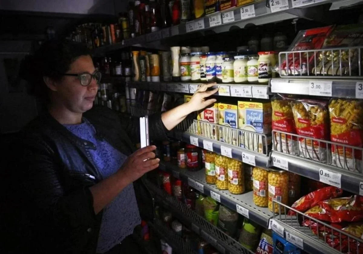 A customer illuminates the shelves of a supermarket with her mobile phone during the blackout
