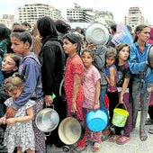 NIños y adultos hacen cola para conseguir algo de comida en Gaza.