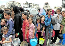 NIños y adultos hacen cola para conseguir algo de comida en Gaza.