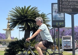 Un hombre monta en bicicleta junto a un termómetro de calle que marca 39 grados este lunes en Sevilla.