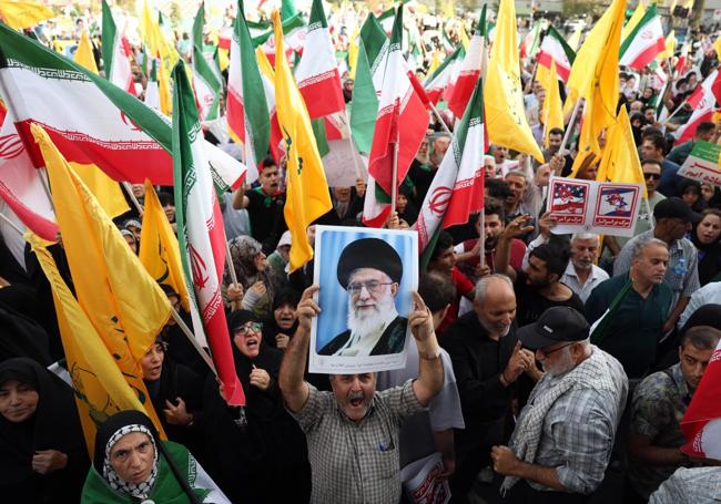 Un iraní sostiene un retrato del ayatolá Ali Jamenei, entre banderas nacionales durante la manifestación de este martes en Teherán.