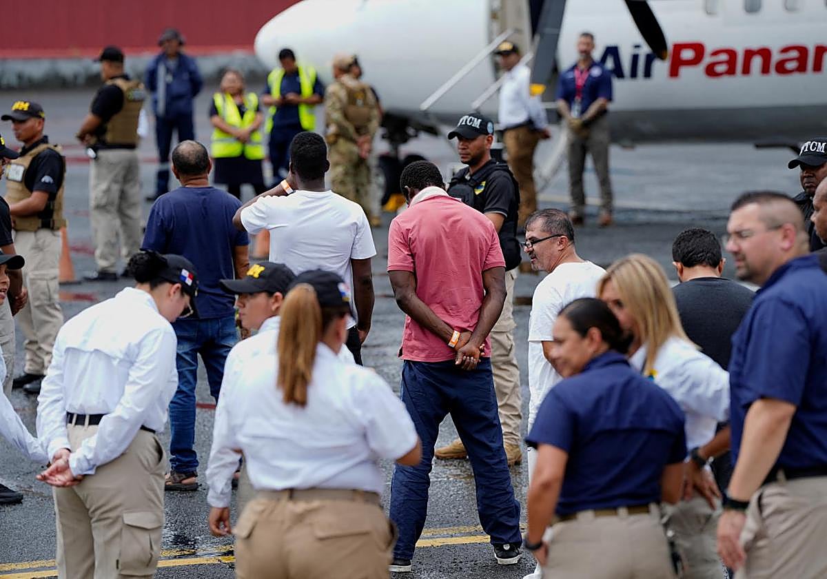 Agentes federales vigilan a migrantes antes de ser deportados de Estados Unidos a Colombia.