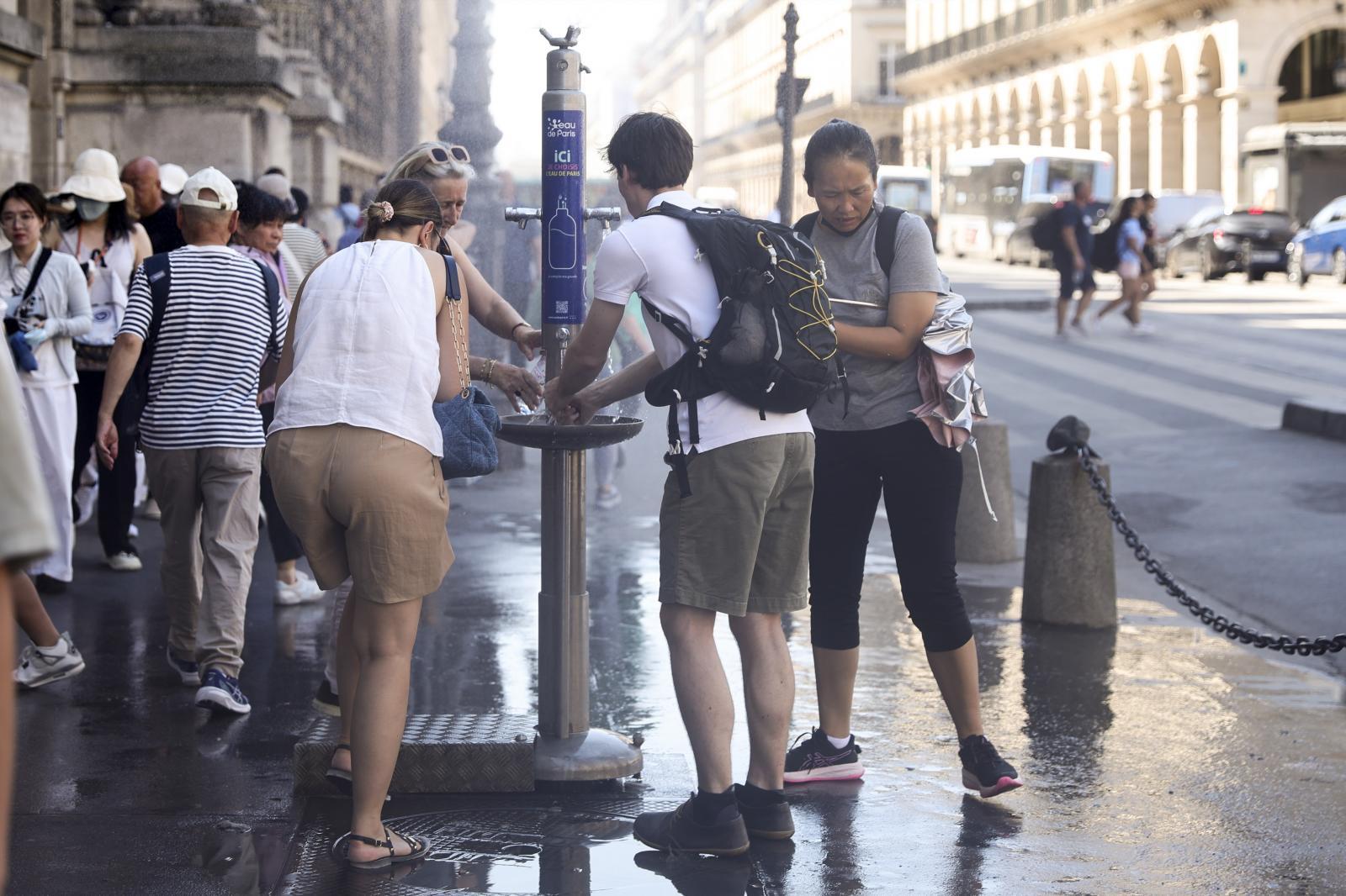 Varias personas se refrescan en uno de los surtidores de agua fría instalados en las calles de París.