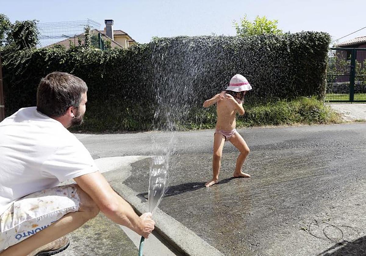 Un padre rocía agua con una manguera a su hija para refrescarla por las altas temperaturas.