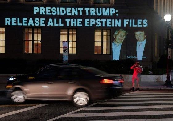 Un hombre cruza un paso de cebra enfrente de un anuncio que pide «Presidente Trump, publica todos los archivos de Epstein.