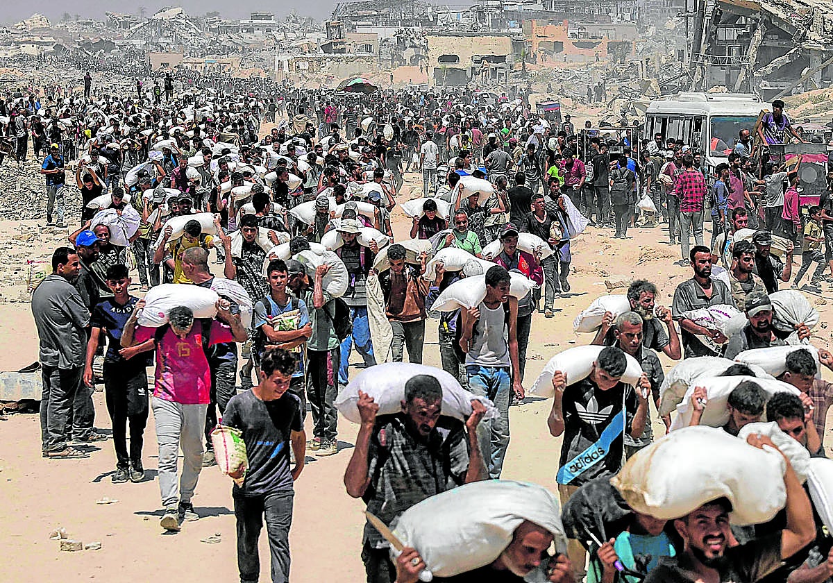 Ciudados de Gaza cargan a hombros con sacos de comida en un centro de reparto.