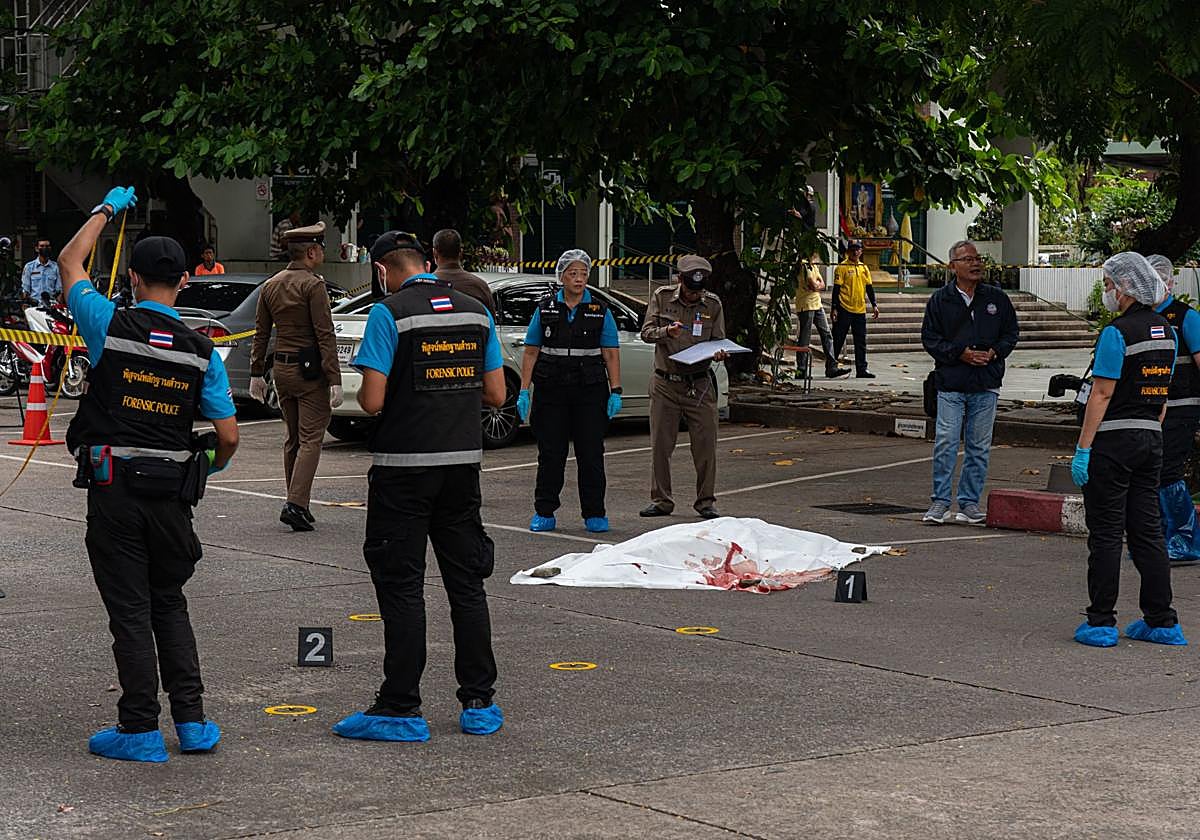 Agentes custodian un cadáver en la escena de un tiroteo en un mercado de Bangkok.