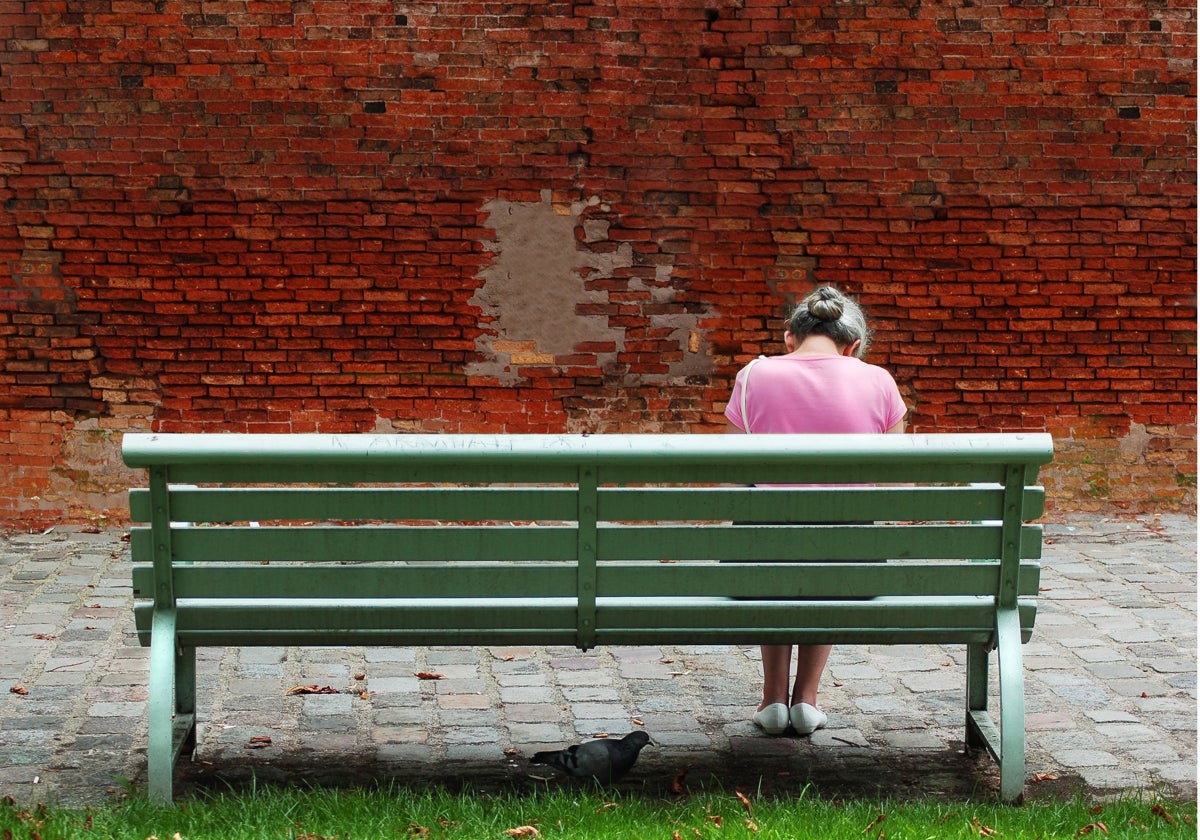 An elderly woman sitting alone on a street bench.