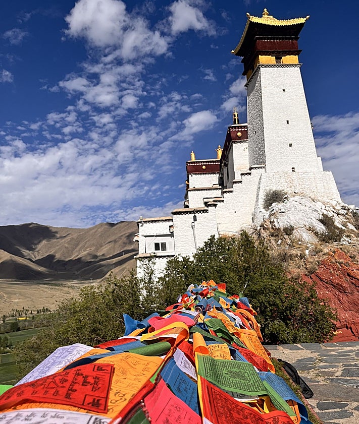 Imagen secundaria 2 - Banderas de oración y una peregrina con su rosario y su móvil en el palacio-castillo de Yumbulakang o Yumbu Lha Khang, el primer edificio construido en Tíbet según la tradición budista.