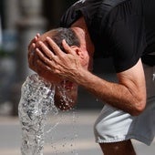 Una hombre se refresca en un surtidor para paliar el calor sofocante.