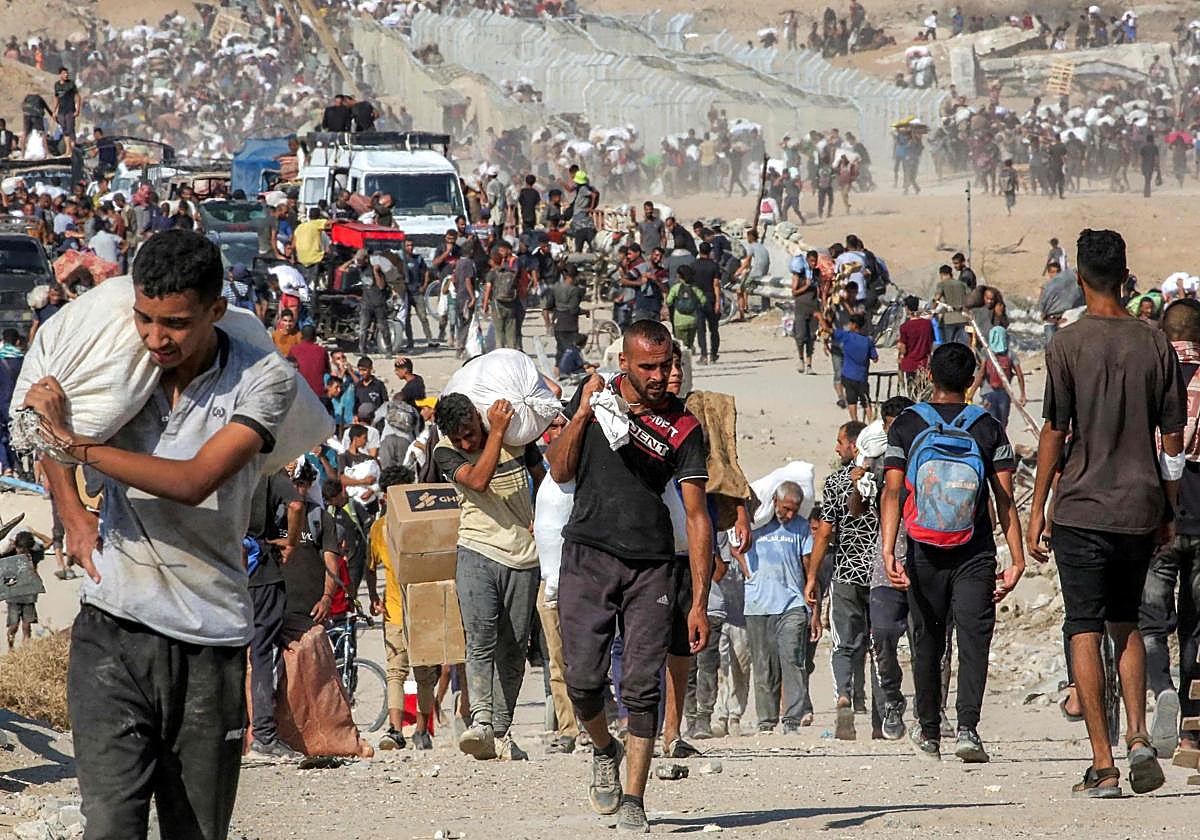 Dos jóvenes caminan con sacos de ayuda humanitaria a los hombros en Gaza.