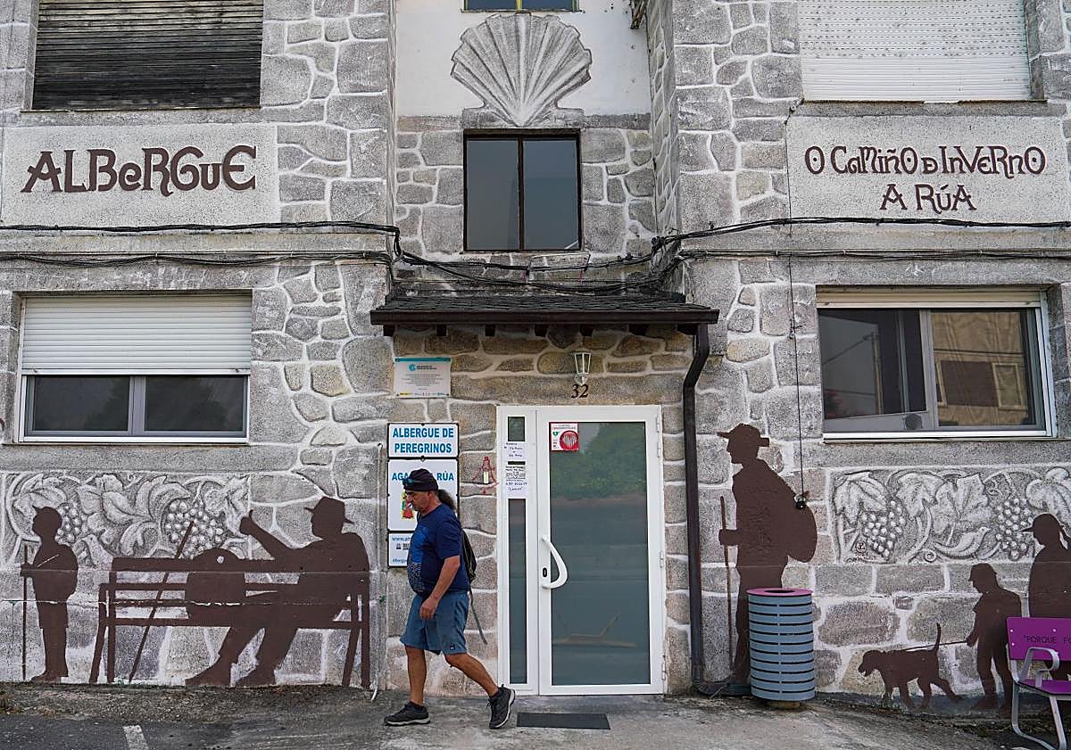 Imagen principal - Arriba entrada al albergue de A Rúa. Abajo, uno de los dormitorios casi vacíos donde pernoctan los peregrinos. A la derecha, Montse Pérez descansa junto a su mochila después de terminar la etapa del día.