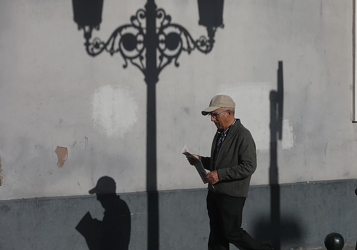 Hombre jubilado pasea por la calle con periódico en mano.