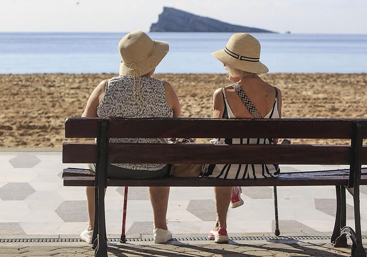 Dos mujeres disfrutan del buen tiempo sentadas ante la playa de Levante de Benidorm.