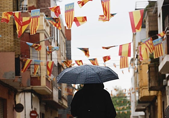 Un hombre pasea con un paraguas bajo los banderines colgados en Catarroja este 9 de octubre, Día de la Comunitat Valenciana.