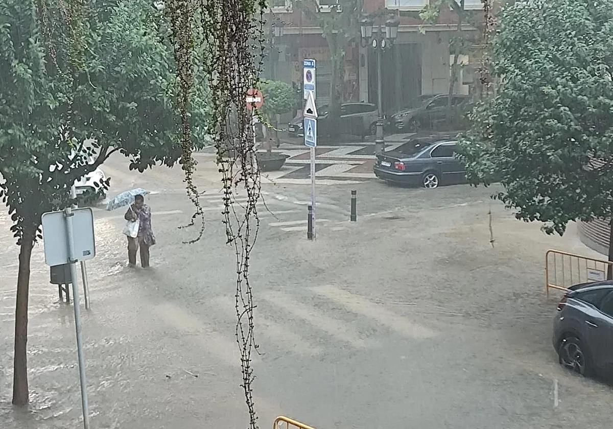 Una mujer intenta cruzar la carretera en una calle inundada de Gandia.