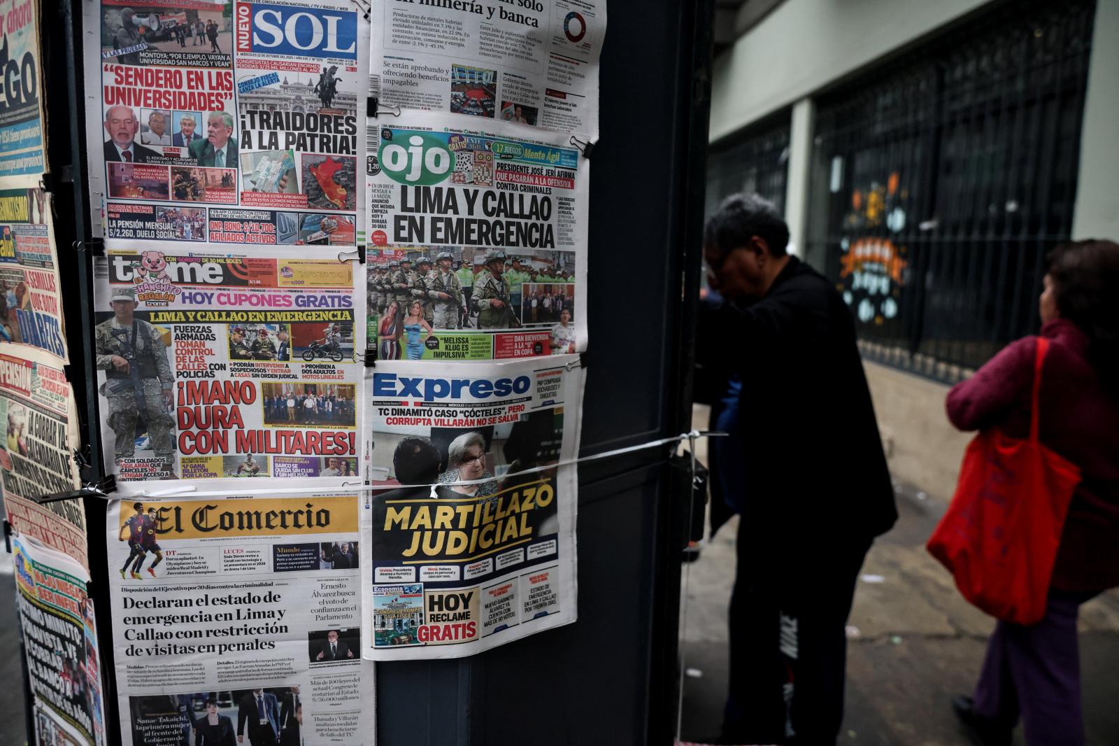 Viandantes caminan frente a un quiosco de periódicos cuyas portadas anuncian la medida de excepción decretada por el Gobierno.