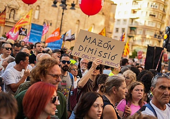 Varias personas con pancartas, y un cartel de Mazón con las manos rojas, durante una manifestación para reclamar la dimisión del presidente de la Generalitat.