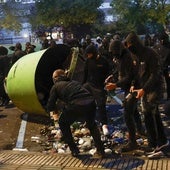 Jóvenes encapuchados recogen botellas de un cubo de basura.