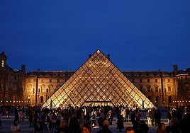 La gente camina cerca de la pirámide de cristal del museo del Louvre.