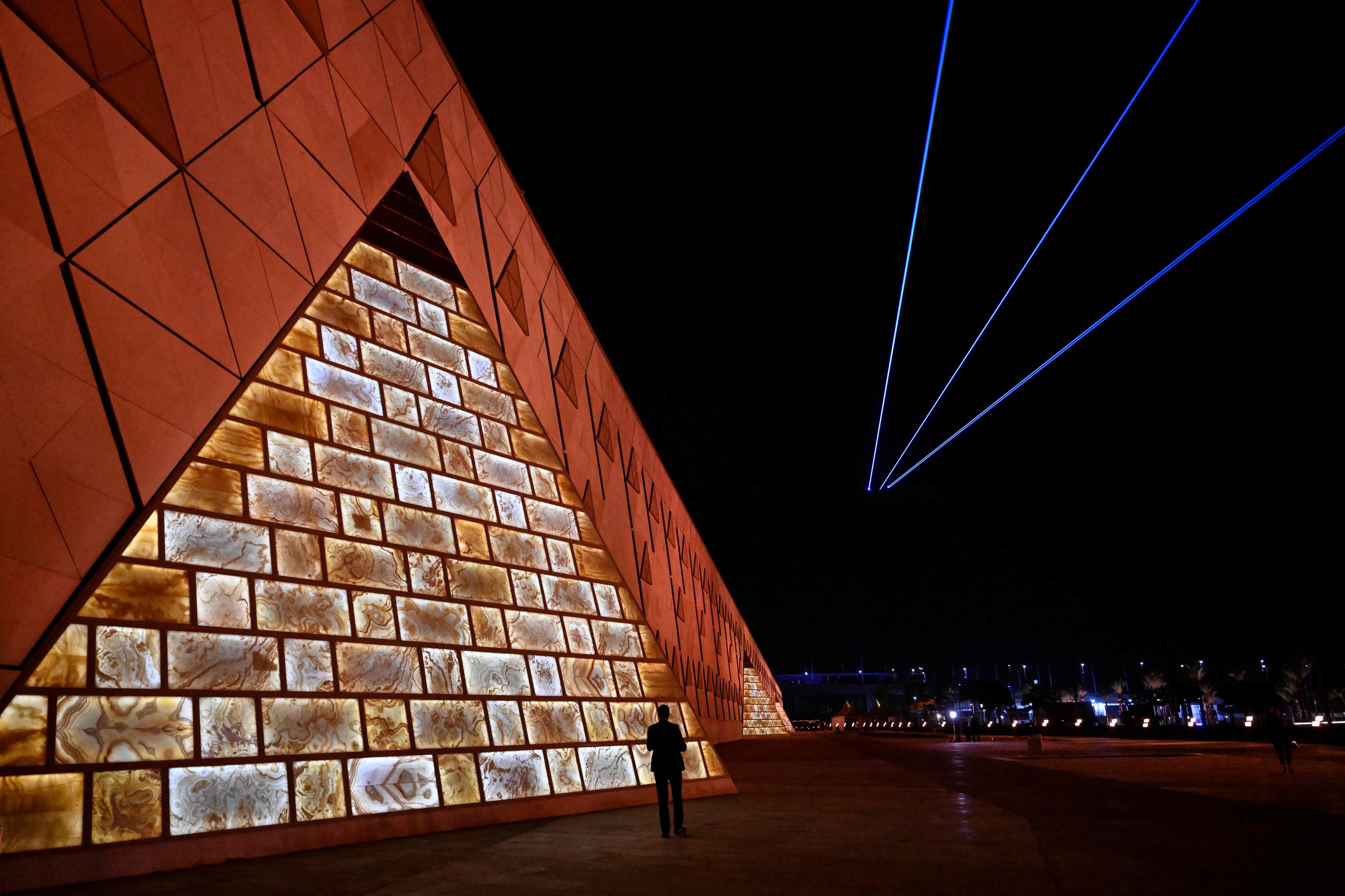 Un hombre camina por los terrenos del Gran Museo Egipcio (GEM) mientras los láseres iluminan el cielo.
