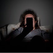 Un adolescente navega con el móvil en la oscuridad nocturna de su habitación.