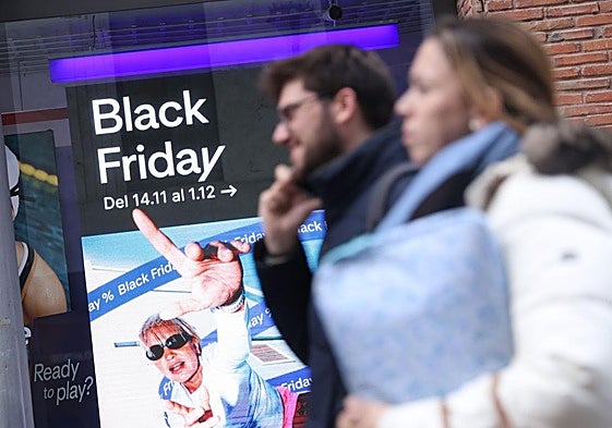 Una pareja pasea por el centro de Valladolid en frente de una tienda que promociona sus descuentos del Black Friday.