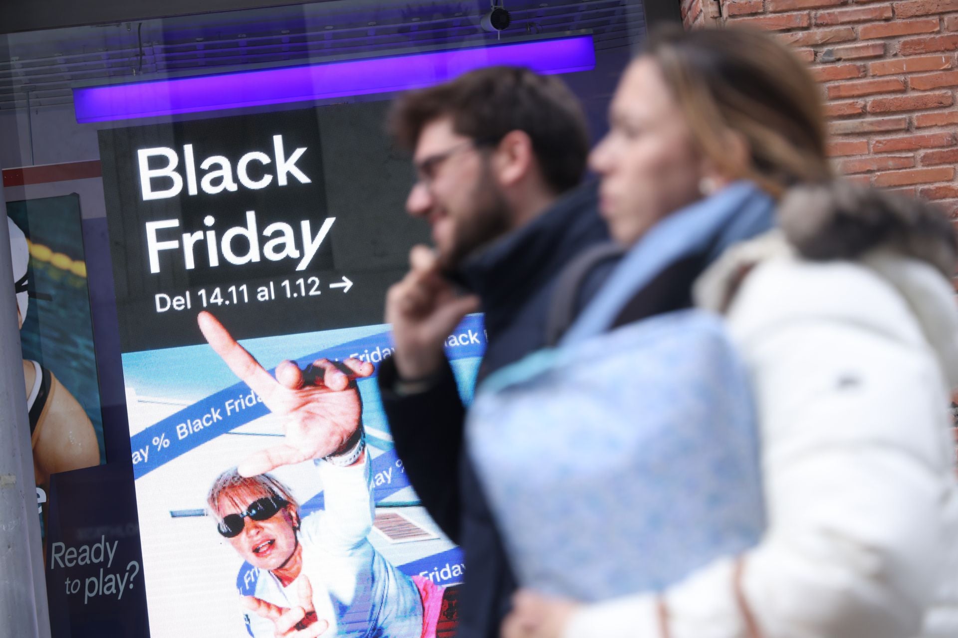 Una pareja pasea por el centro de Valladolid en frente de una tienda que promociona sus descuentos del Black Friday.