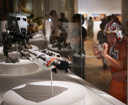 Imagen secundaria 1 - Arriba, dos visitantes junto a un Bansky, debajo un fan de 'Star Wars' fotografía una de las maquetas y dos niñas, junto a un R2D2.