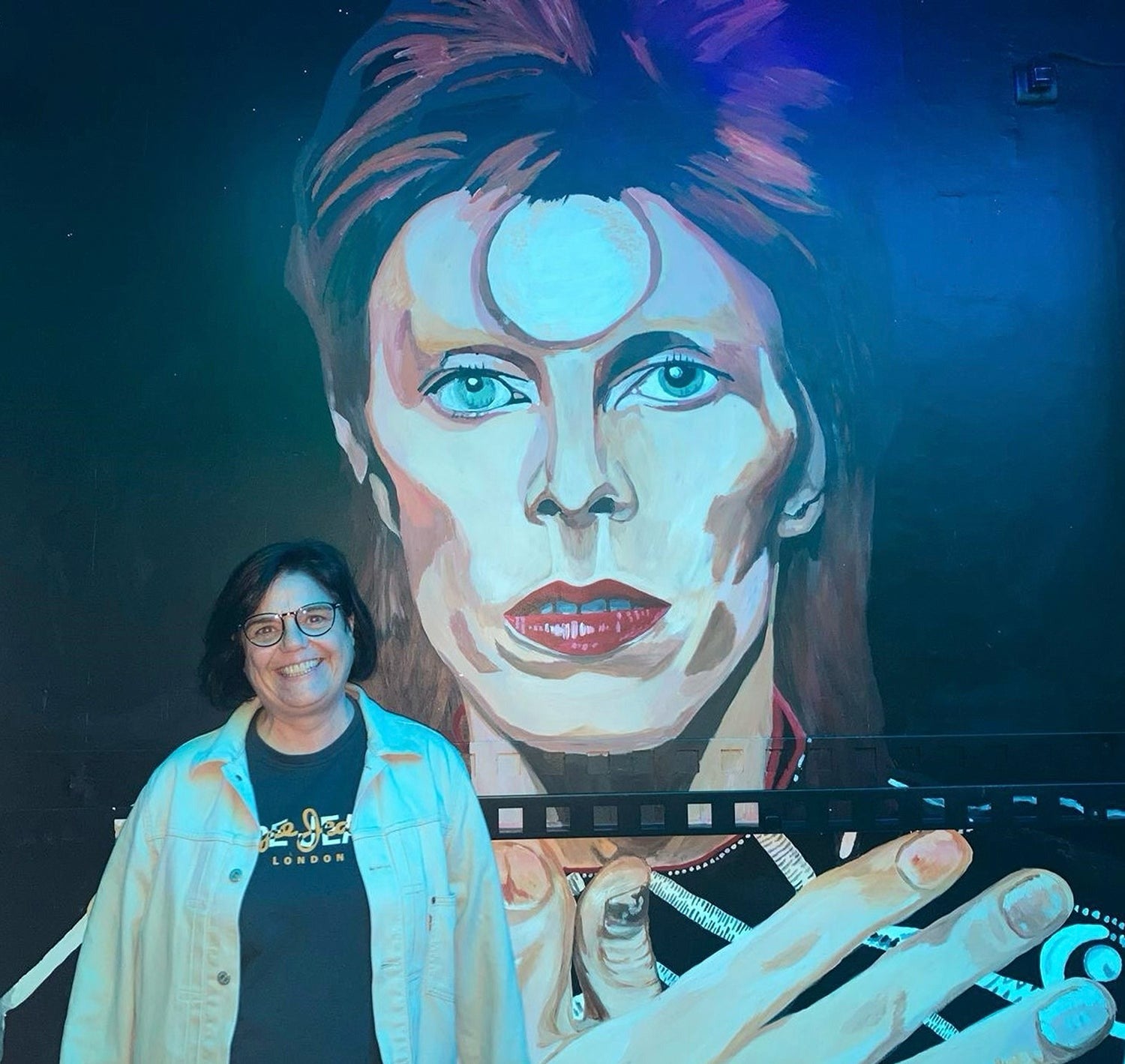 Lali Moldes junto a la pintura de David Bowie de su local. SIX